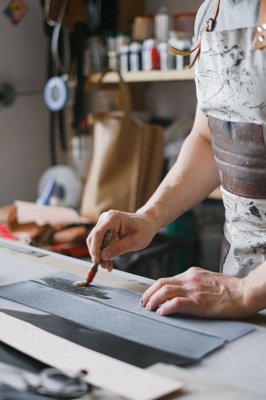 An artisan brushing a finish onto leather panels at a workshop bench