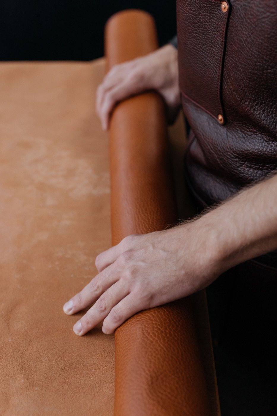 A craftsman’s hands smoothing a hide of soft suede beside a rolled leather edge
