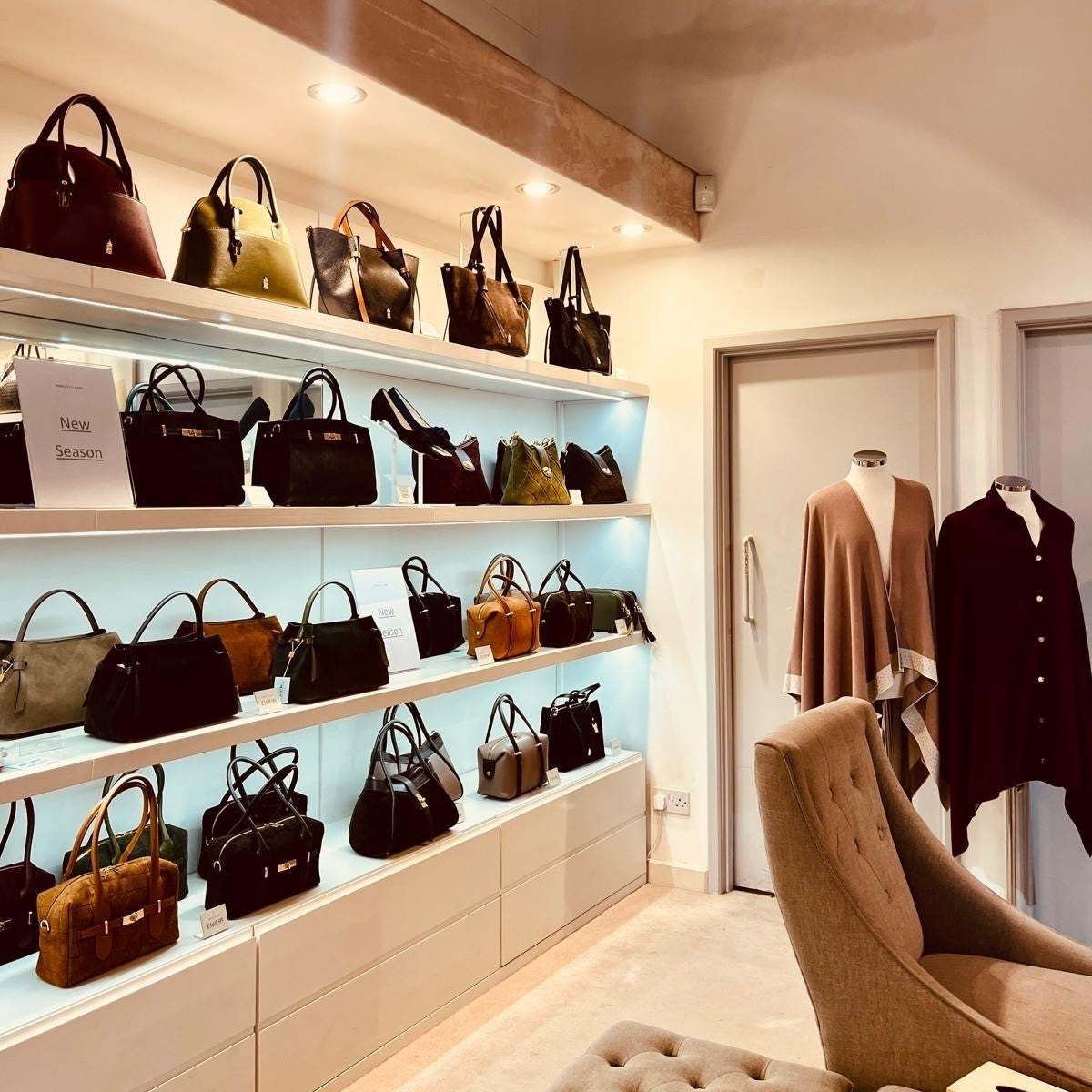 Inside the Franchetti Bond store: handbags on lit shelves, a New Season sign, ponchos on mannequins and a tufted armchair